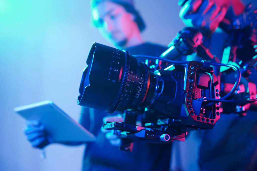 Cinema camera on a rig in a studio lit in blue and pink, with an operator behind it