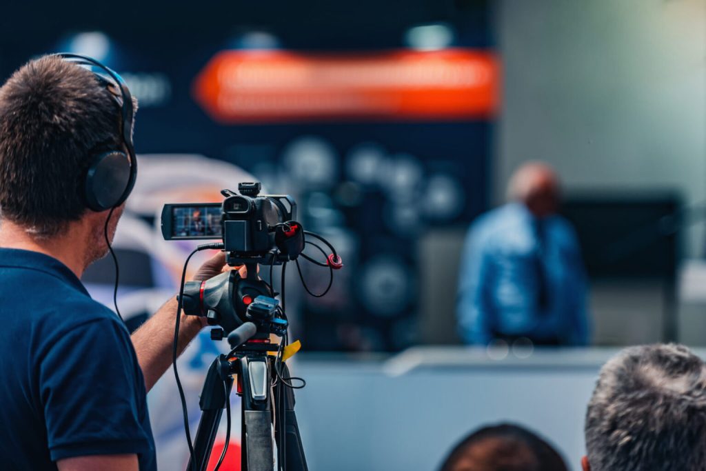Camera operator with headphones filming a speaker at a press conference