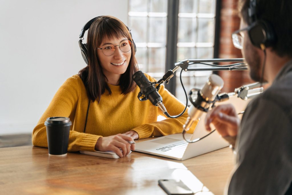 Two podcasters talking into microphones in a studio